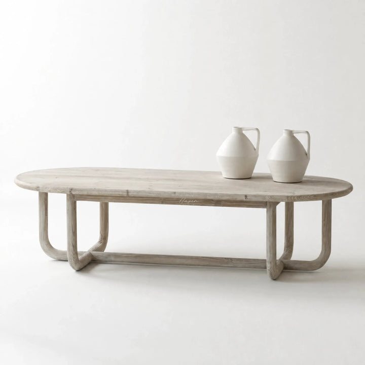 Jones Coffee Table in light chalk-washed wood with curved silhouette, shown with three white ceramic vases.