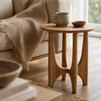 Elin Oak Side Table with sculptural base and circular top in natural oak beside a beige sofa