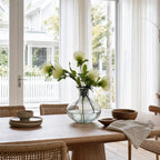 Ingrid Glass Vase with smoky hue, suspended bubbles and petal-shaped rim, displayed with stems on a dining table.