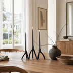 MUUBS Aion Candleholder Set/2 in black cast iron with tree-branch silhouettes on a wooden dining table.