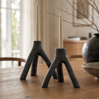 MUUBS Aion candleholder set/2 in black cast iron with tree-branch style bases and tall ivory candles.