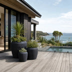 Piha Planters Set/3 in premium stone composite, sculptural dark pots on a coastal deck with greenery and sea view.