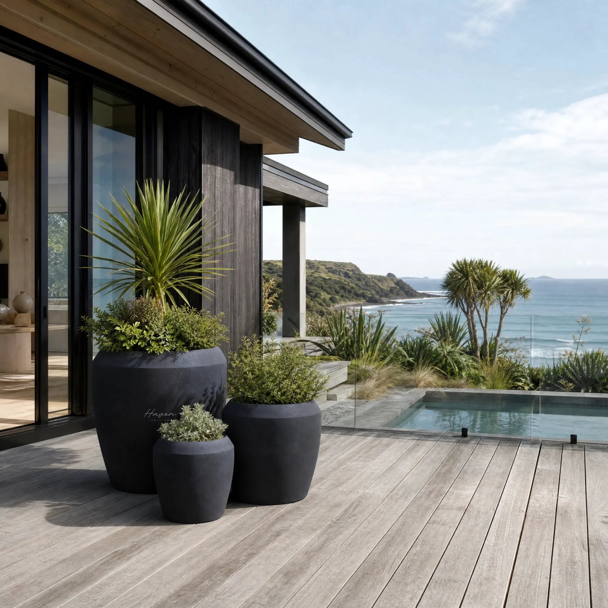 Piha Planters Set/3 in premium stone composite, sculptural dark pots on a coastal deck with greenery and sea view.