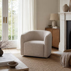 Annika Swivel Chair with a soft curved silhouette in beige upholstery beside a fireplace.