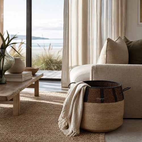 Aarna Basket: handwoven from seagrass with cream body, brown rim and chocolate stripes beside a sofa.