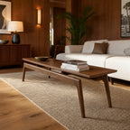 Rowan Coffee Table in solid American Ash with mid-century lines, shown with stacked books in a warm living room.
