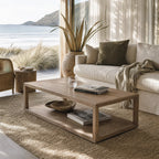 Driftwood Coffee Table in solid ash with open lower shelf, set in a coastal living room by the ocean.