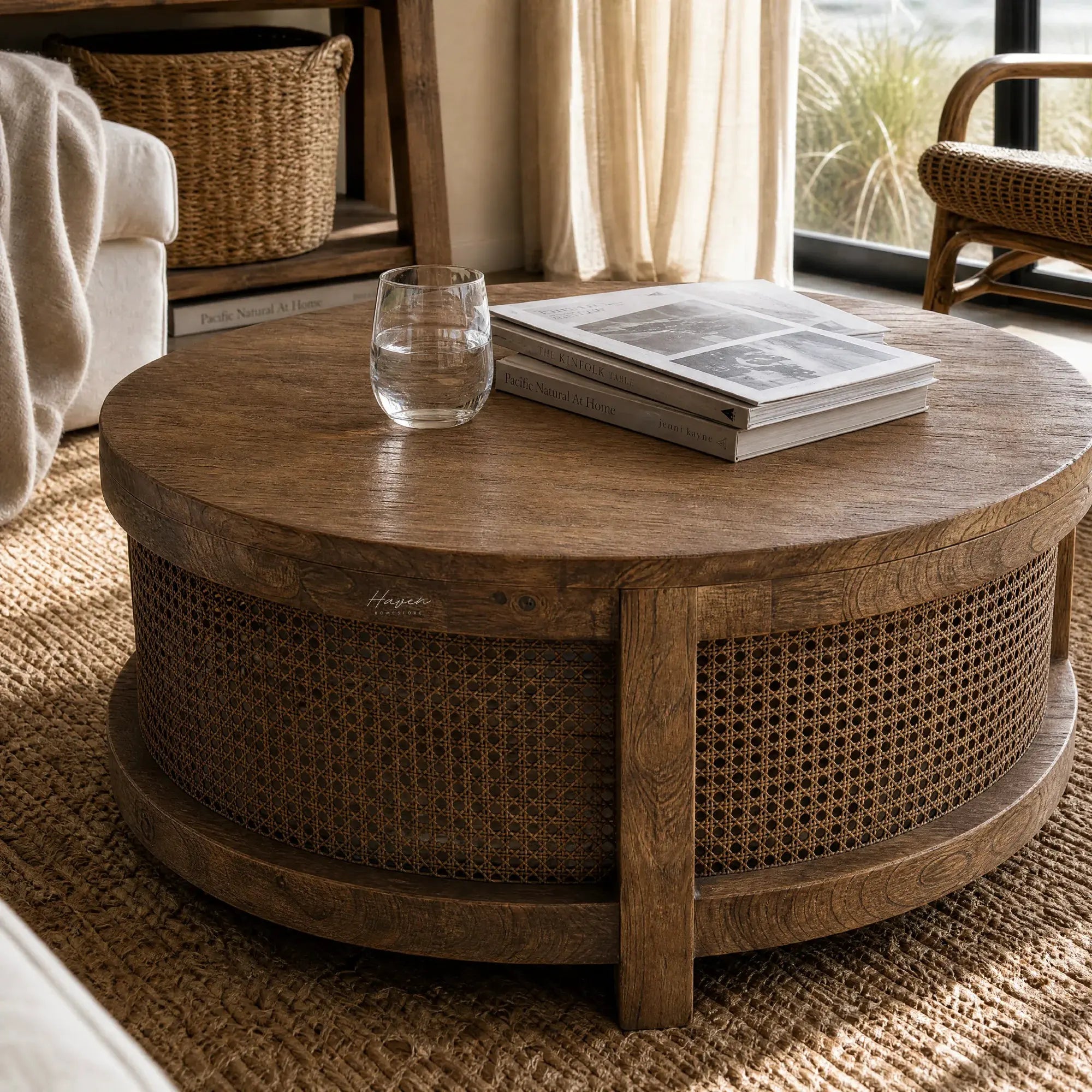 Ubud Coffee Table with bleached elm top and handwoven rattan base, round, in warm living room with glass and magazines.
