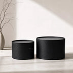 Daven Coffee Table Set/2: two textured black iron nesting coffee tables with a vase and bare branches.