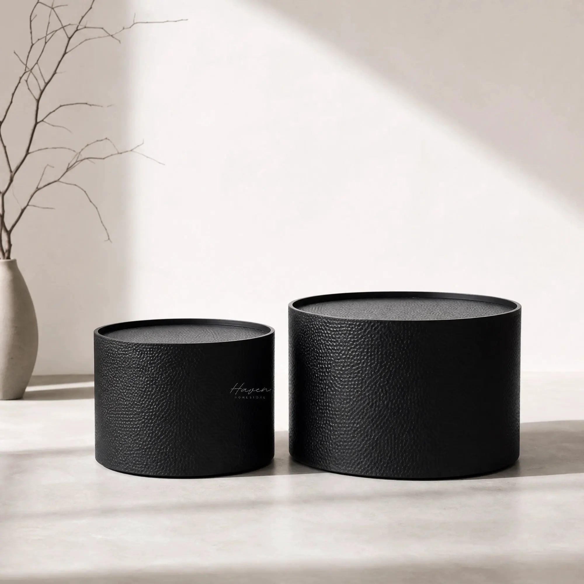 Daven Coffee Table Set/2: two textured black iron nesting coffee tables with a vase and bare branches.