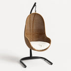Cabana Pod Chair: woven rattan-style wicker seat with white cushion on a black metal stand.