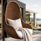 Cabana Pod Chair: woven wicker hanging chair with beige cushion on outdoor deck