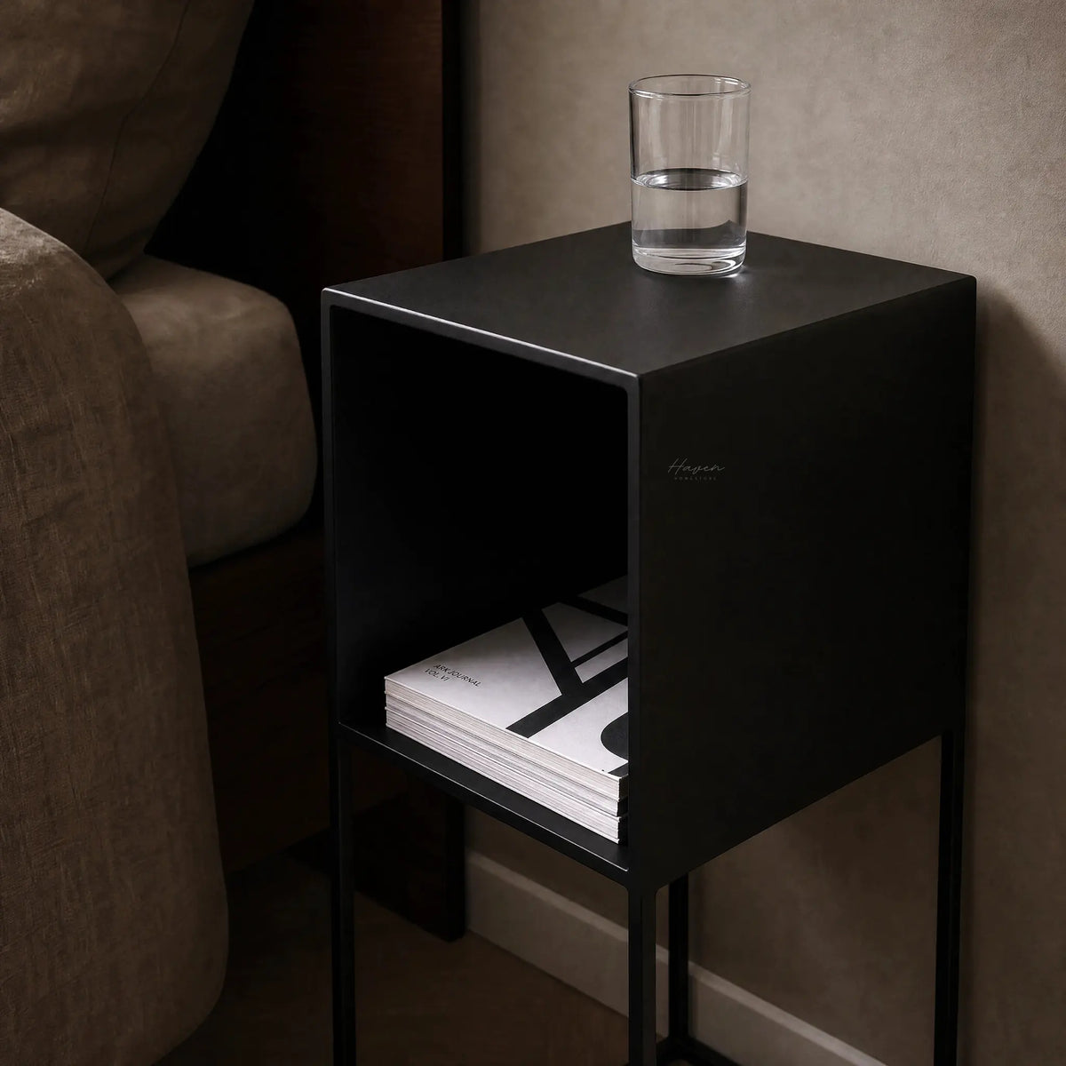 STUDIO Bedside Cabinet Small in black metal with an open shelf and a glass of water on top.