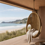Rattan Pod Chair hanging on a wooden deck, handwoven natural rattan cocoon seating by the sea.