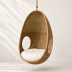 Rattan Pod Chair: hanging handwoven cocoon seat in natural rattan with white cushion.