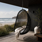 Check Pod Chair hanging on a deck with coastal view, woven black mesh over galvanised metal frame, and beige blanket.
