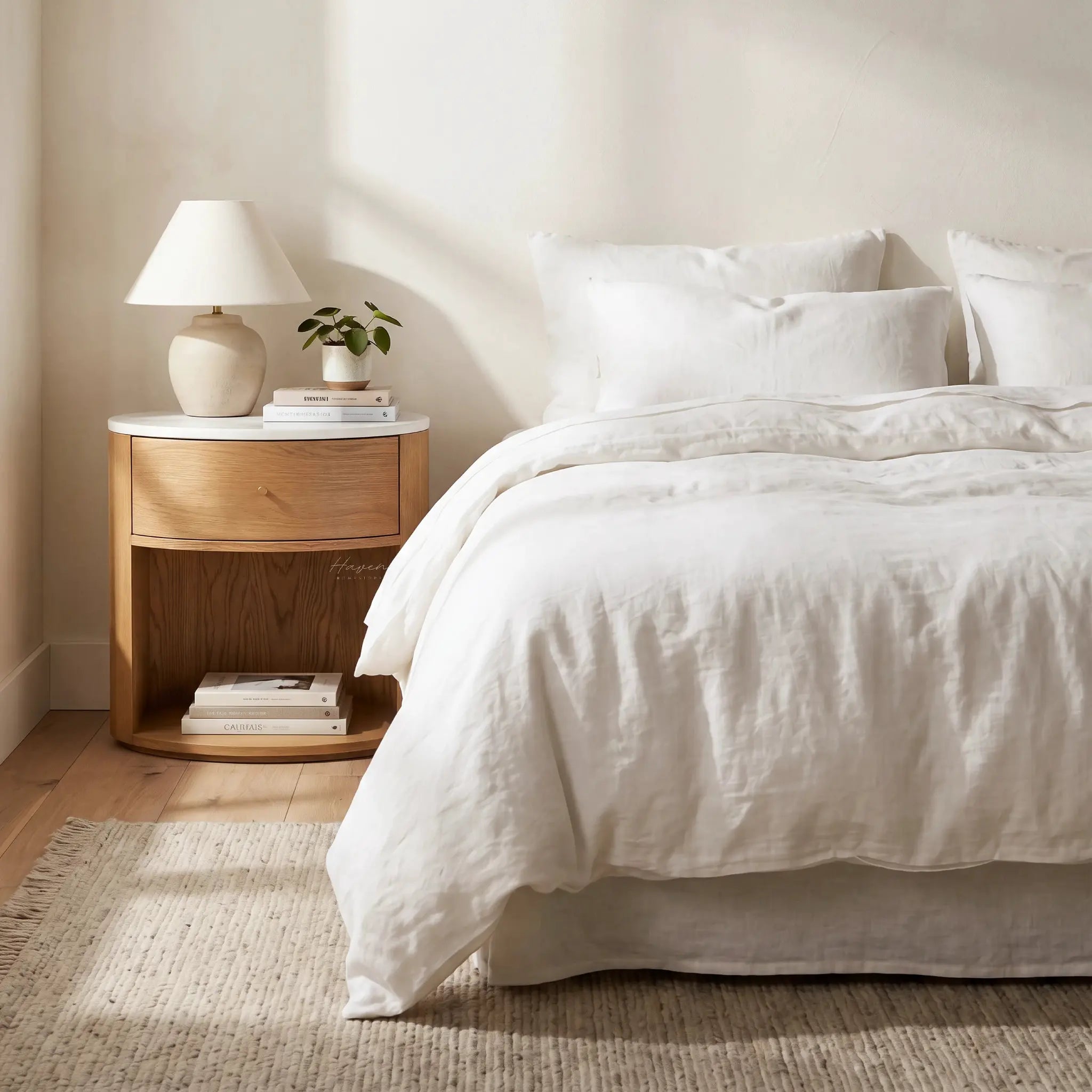 Dana Bedside Table with warm oak, marble top, and rounded silhouette beside a bed.