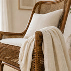 Albany Chair handwoven in natural rattan with curved silhouette, beige cushions and draped throw.