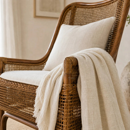 Albany Chair handwoven in natural rattan with curved silhouette, beige cushions and draped throw.