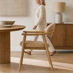 Celine Dining Chair with a solid ash frame and rounded beige upholstery beside a round wooden dining table.