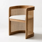 Cove Cane Chair with curved oak frame, woven rattan panels, and softly cushioned seat.