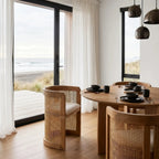 Cove Cane Chairs with curved oak frames, woven rattan panels, and softly cushioned seats around a round dining table.