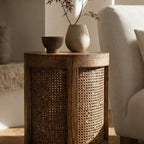 Cala Side Table in elm with natural rattan panels, featuring dark cup and pale vase with branches.
