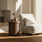 Cala Side Table in warm elm with natural rattan panels beside a neutral living room seating area.