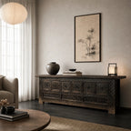 Nomad Coffer Blackened carved dark cabinet on a console in a moody living room with vase and artwork.