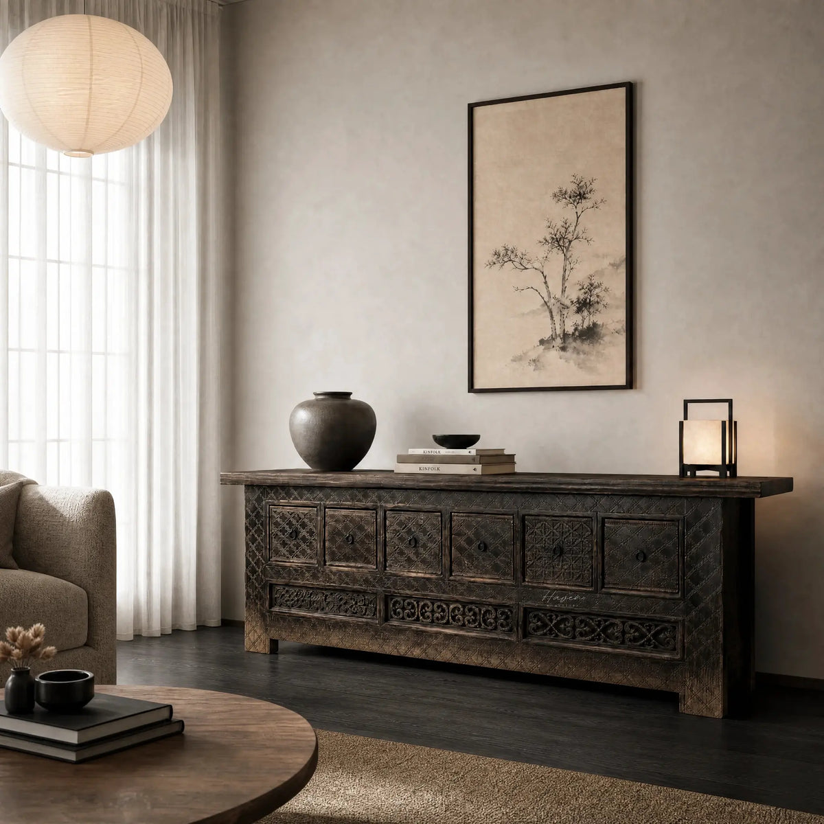 Nomad Coffer Blackened carved dark cabinet on a console in a moody living room with vase and artwork.