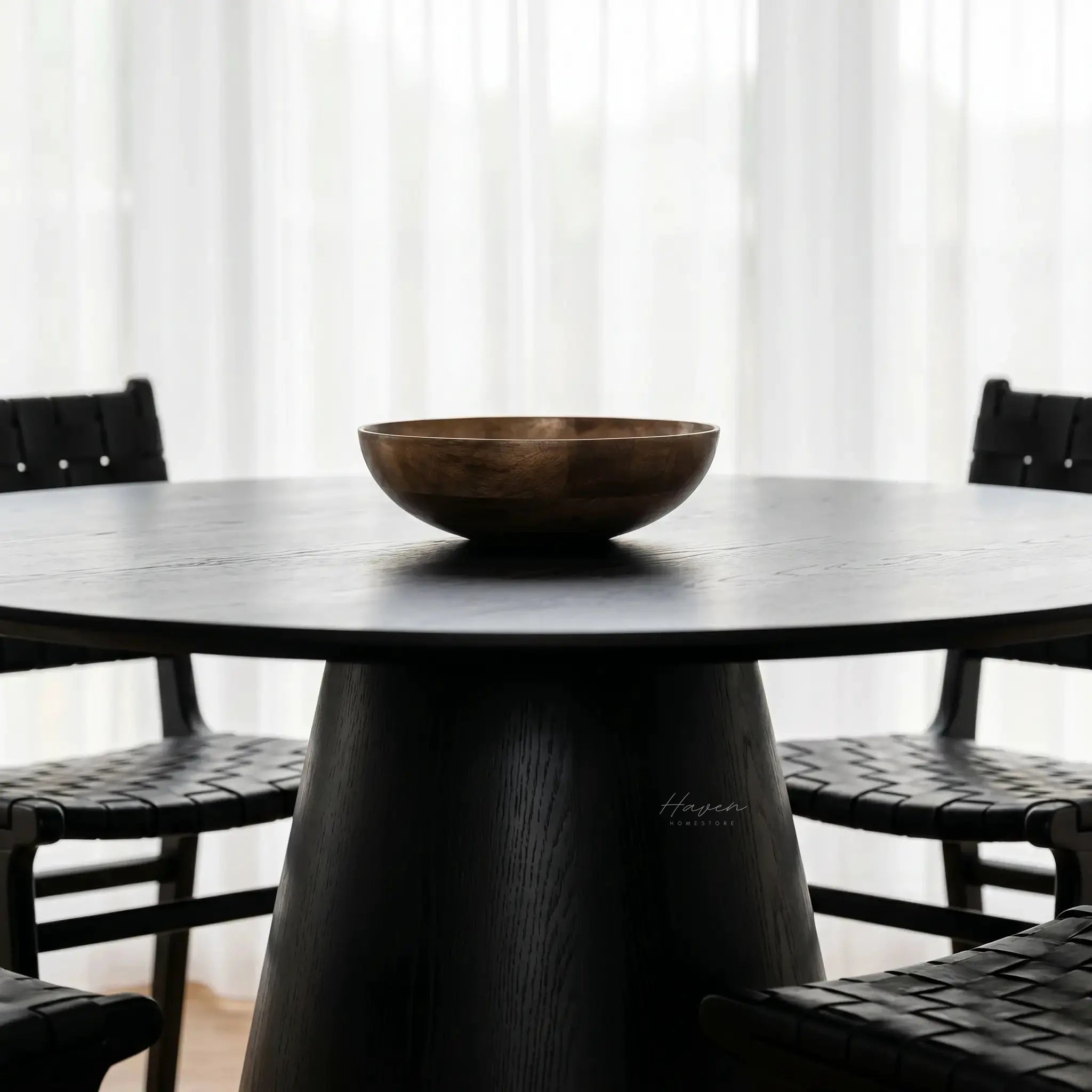Charlie Dining Table with bold pedestal base and rounded top in black oak veneer, shown with a wooden bowl.