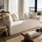 Cove Slipcover Sofa - 3 Seat in beige linen-cotton with plush cushions in a sunlit coastal living room.