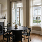 Sora Dining Table - Black: round top with a fluted pedestal base, in a sunlit dining room with black chairs.