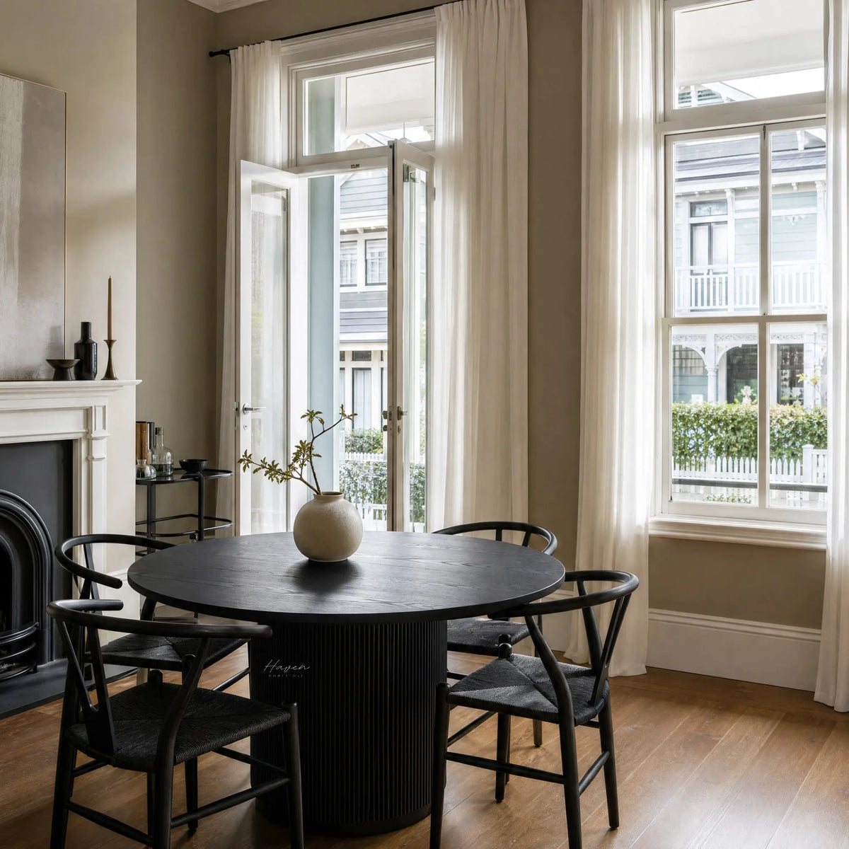 Sora Dining Table - Black: round top with a fluted pedestal base, in a sunlit dining room with black chairs.