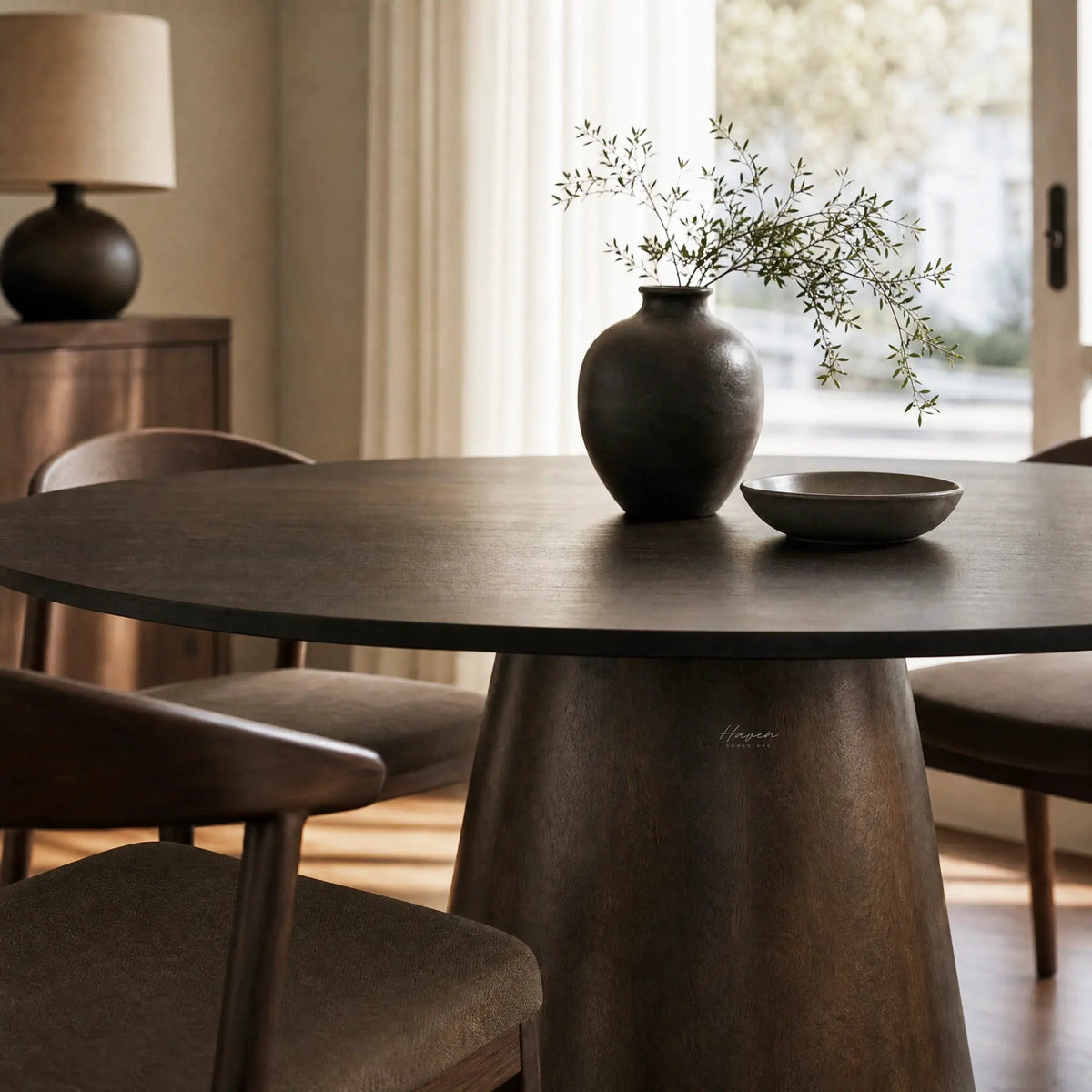 Mika Dining Table in dark mango wood with a round top and tapered pedestal, styled with a ceramic vase.