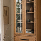 Halden Display Cupboard in solid oak with veneer panels and glass doors, showcasing ceramics and books.