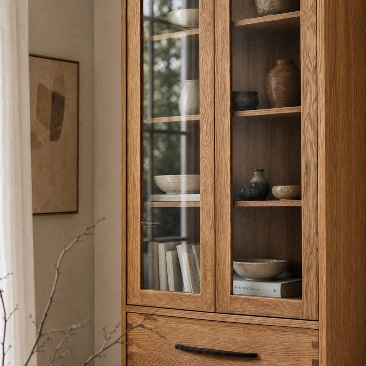 Halden Display Cupboard in solid oak with veneer panels and glass doors, showcasing ceramics and books.