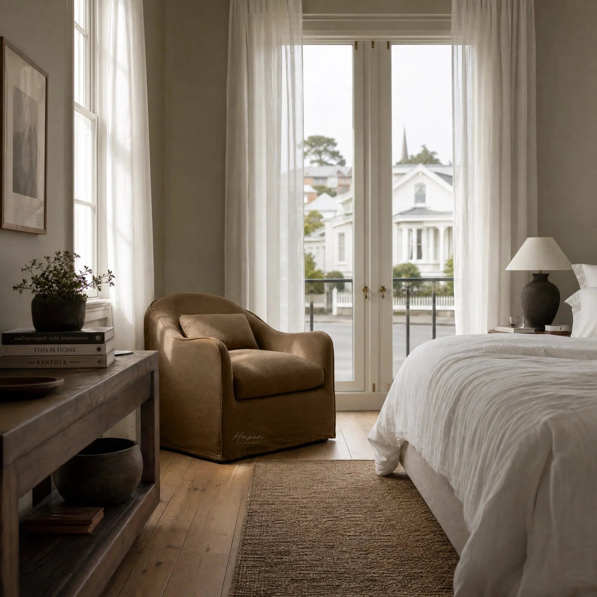 Softly curved Nella slipcover chair in warm Mocha linen positioned in a sunlit bedroom beside sheer curtains.