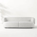 Low profile sofa with a continuous curved back and pale textured upholstery bringing architectural calm to the room.