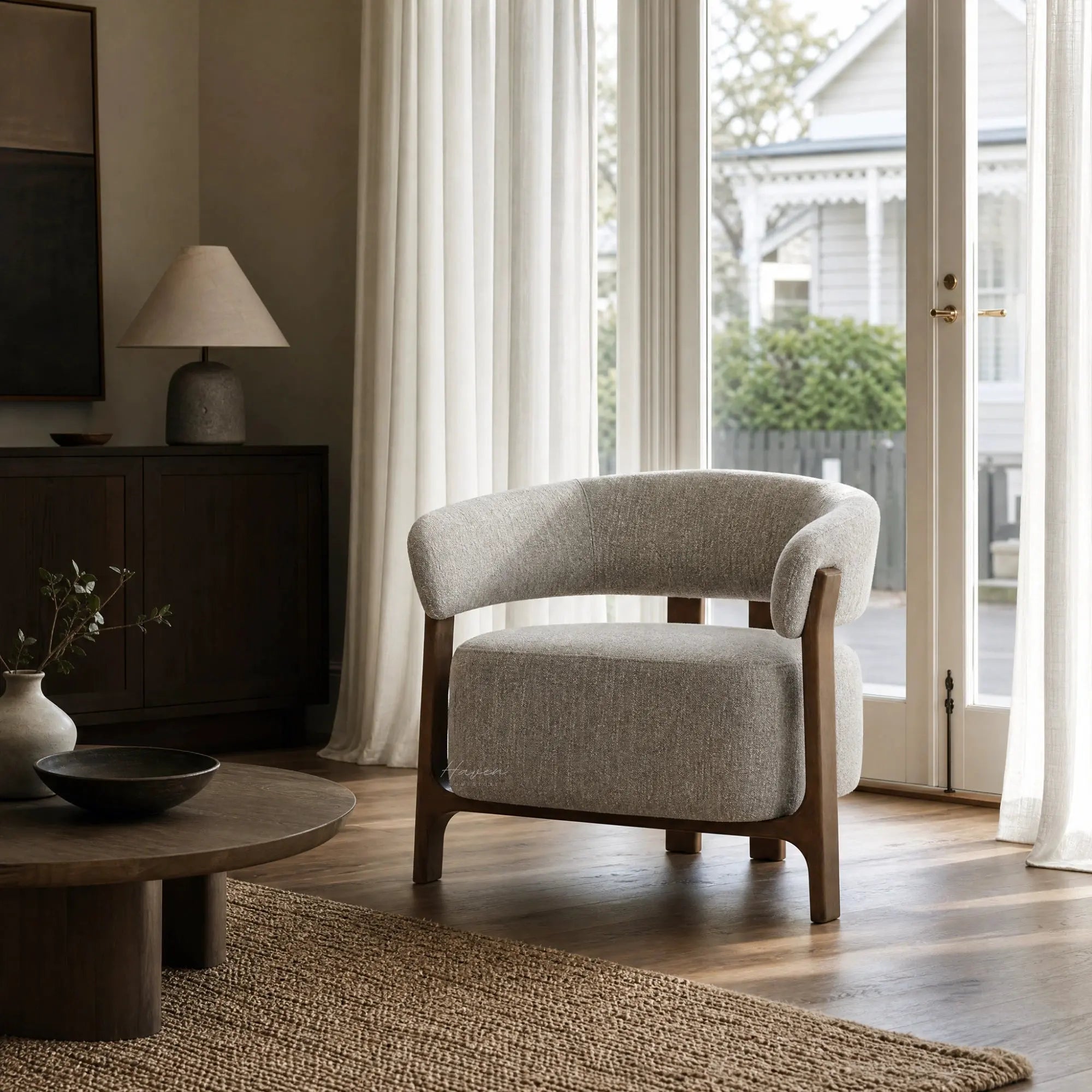 Seki Chair in Pumice fabric features a curved upholstered back and exposed solid ash frame positioned near a window with sheer curtains.