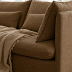 Mocha linen slipcover sofa with loose cushions and textured throw blanket, featuring a relaxed low silhouette.