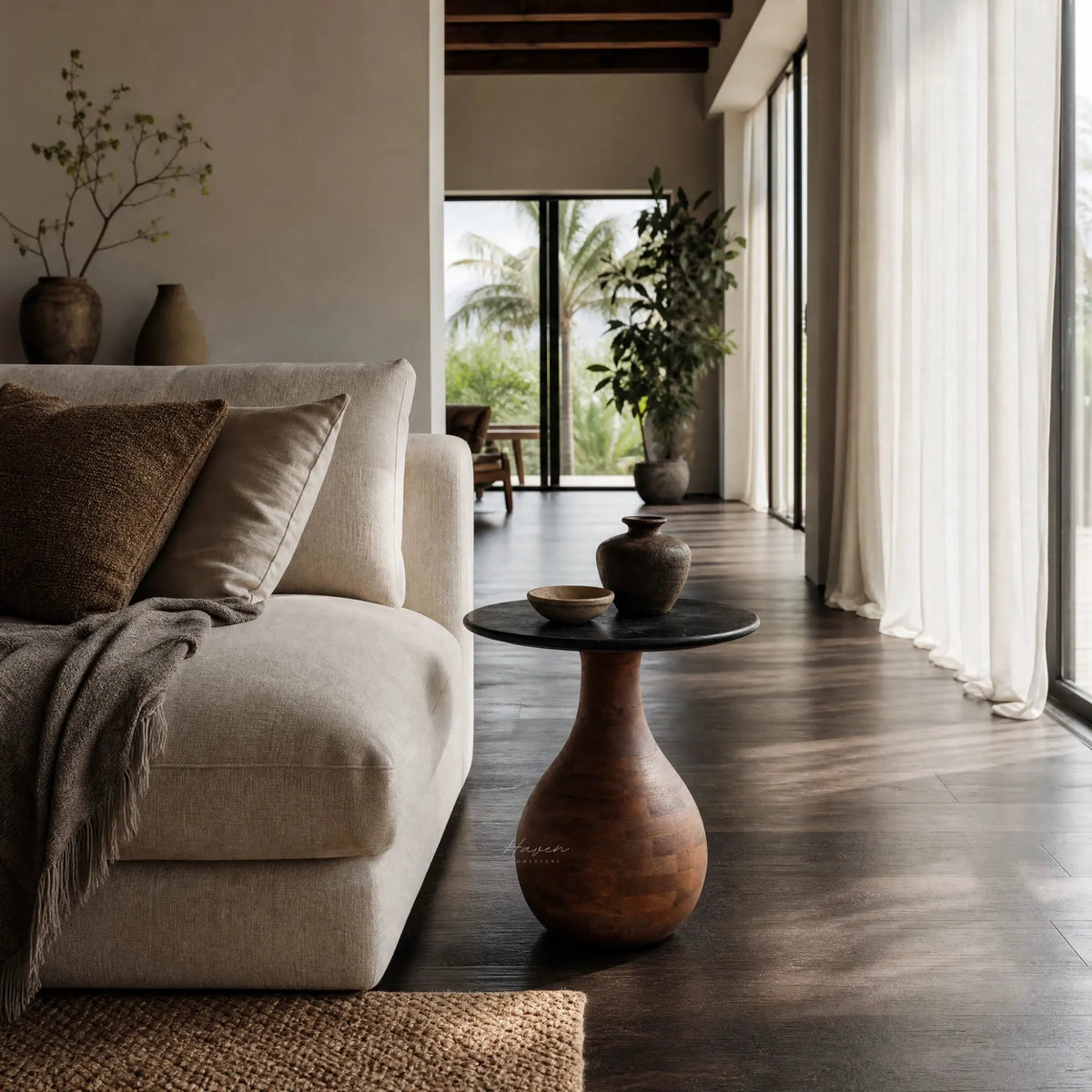 Sculptural side table with a black marble top and tapered mango wood pedestal base beside a beige sofa.