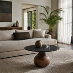 Round coffee table with black marble top and rounded mango wood pedestal base in a living room.