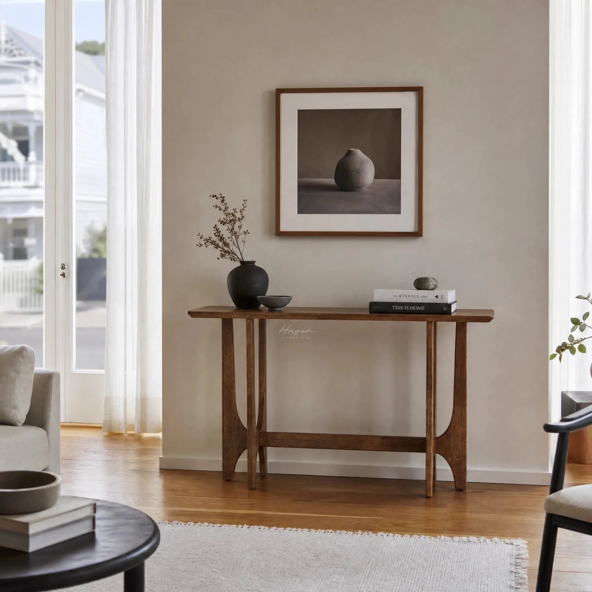 Slender rubber wood Toma Console with open framework and sculpted supports, styled with a vase and books in a bright entryway.