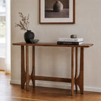 Slender rubber wood console table with open framework and sculpted supports, styled with books and a dark vase against a neutral wall.