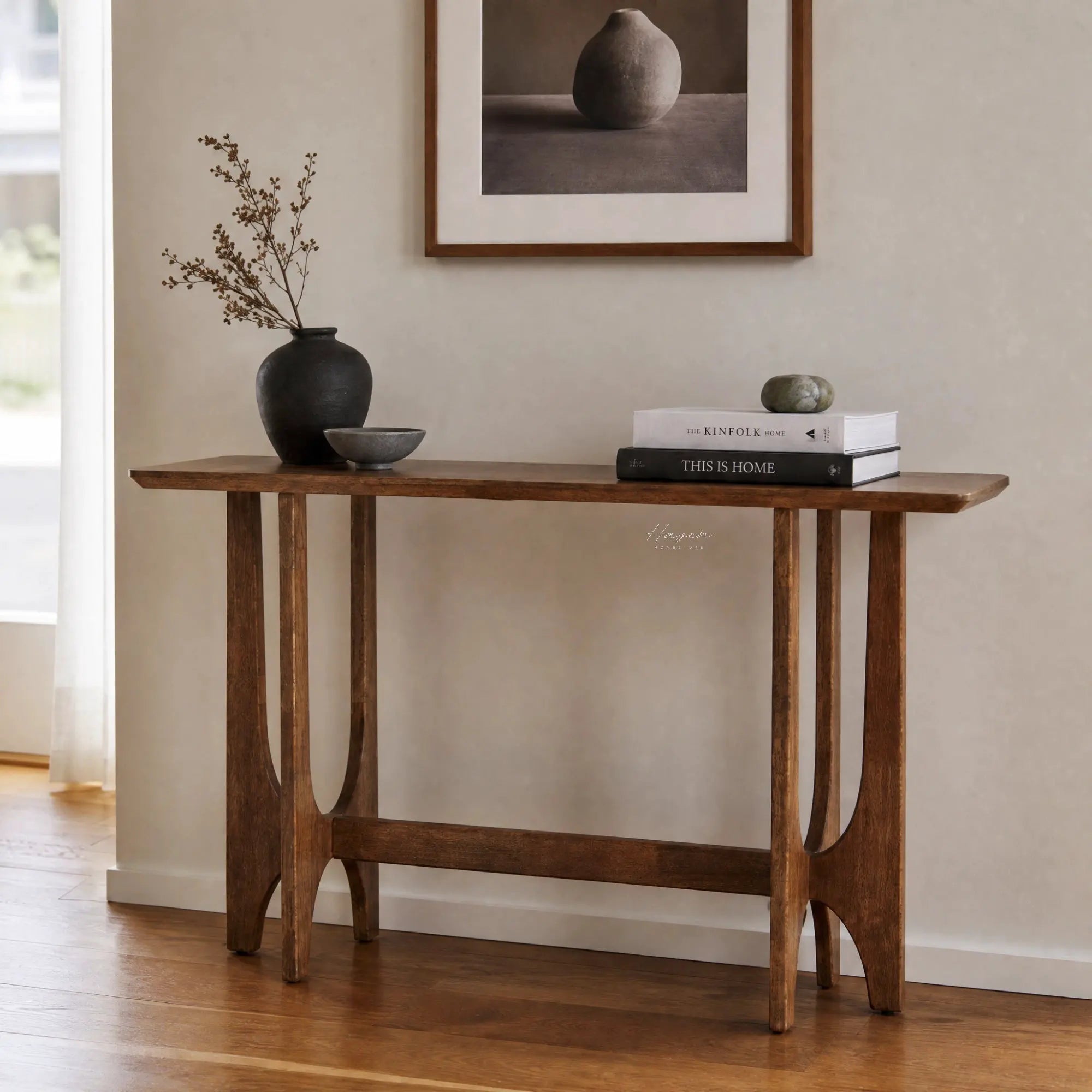 Slender rubber wood console table with open framework and sculpted supports, styled with books and a dark vase against a neutral wall.