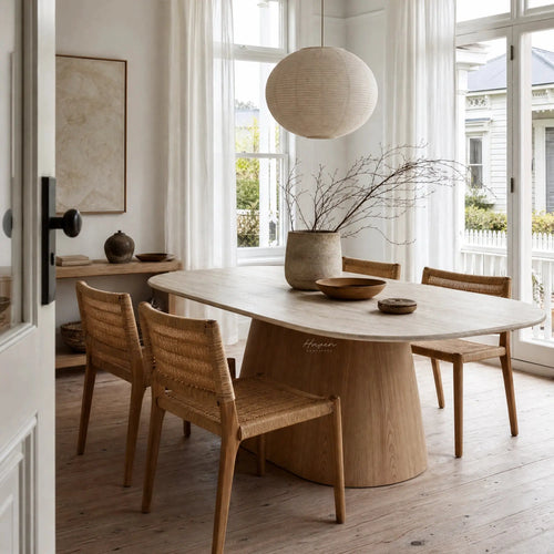 Oval faux marble dining table with a tapered wooden pedestal base and woven chairs in a sunlit room.