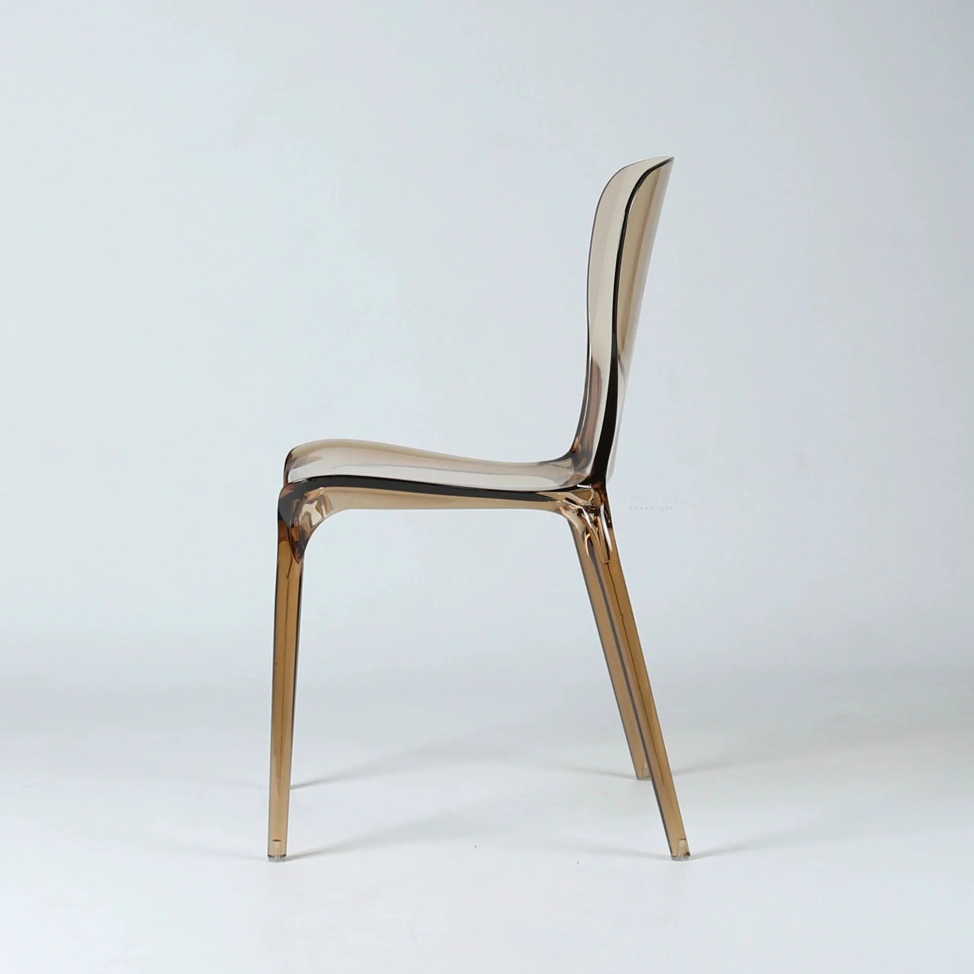 Side view of an amber transparent polycarbonate dining chair with a curved, continuous molded seat and slender legs.