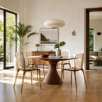 Set of four amber transparent polycarbonate dining chairs with slender legs arranged around a wooden pedestal table in a sunlit room.