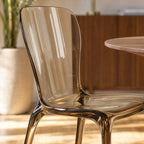 Amber transparent polycarbonate dining chair with a continuous moulded silhouette, softly curved back, and architectural presence.